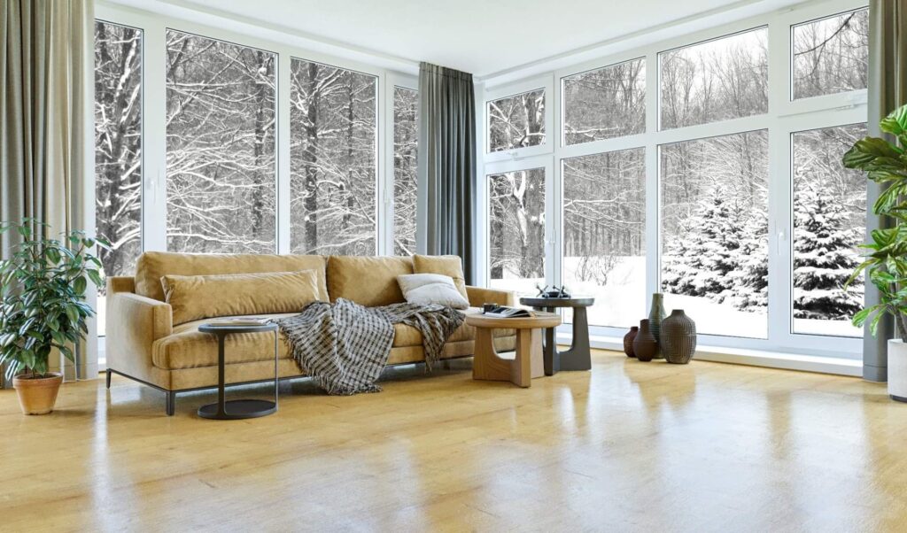 3D-visualisering af lys stue med lodrette panoramavinduer, snedækket skovudsigt, sennepsgul sofa, plaid, sidebord, vaser, bordlampe og varmt trægulv.